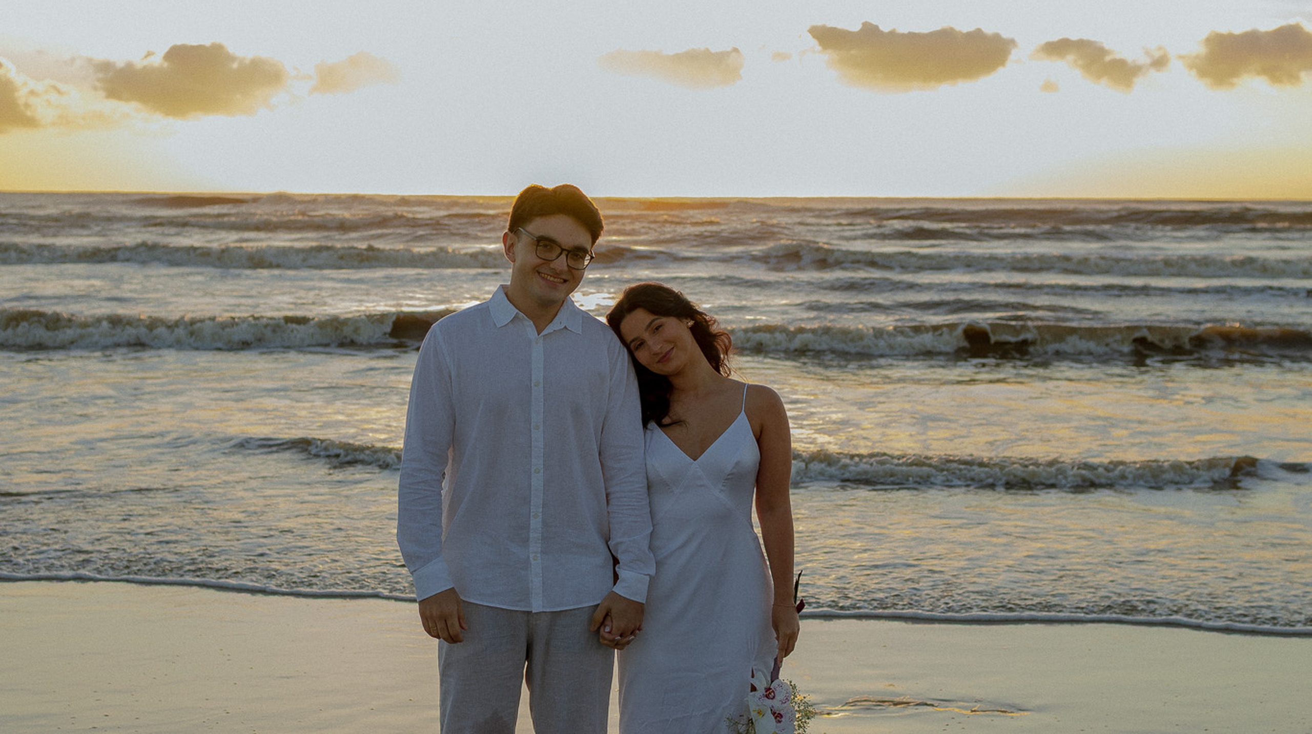 Thassia e Rodrigo de mãos dadas na praia ao pôr do sol